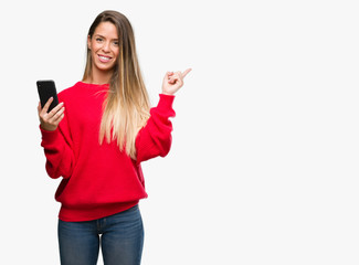Naklejka premium Beautiful young woman using smartphone very happy pointing with hand and finger to the side