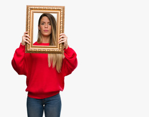 Beautiful young woman holding vintage frame with a confident expression on smart face thinking serious