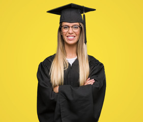Beautiful young woman wearing glasses and graduation robe with a happy face standing and smiling...