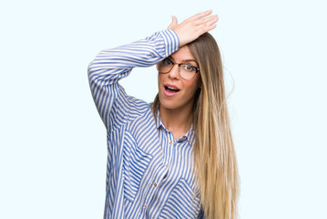 Beautiful young woman wearing elegant shirt and glasses surprised with hand on head for mistake,...