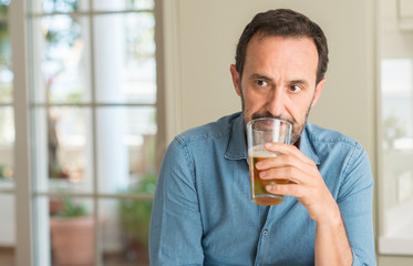 Middle age man drinking beer with a confident expression on smart face thinking serious