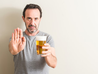Senior man drinking beer with open hand doing stop sign with serious and confident expression,...