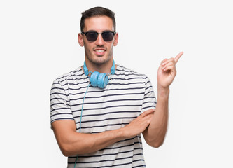 Handsome young man wearing headphones with a big smile on face, pointing with hand and finger to...