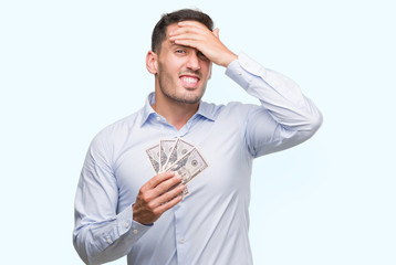 Handsome young man holding money stressed with hand on head, shocked with shame and surprise face,...