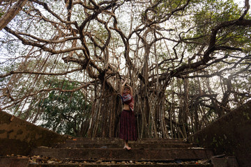 A mighty spreading banyan tree. Asia. The girl has merged with nature. Harmony. Wildness. Brown...