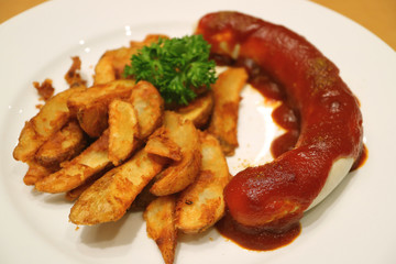 German style Weisswurst sausage with curry tomato sauce and fried potatoes served on white plate