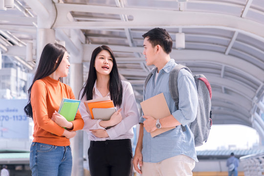 Three Happy Students Walking Towards Camera And Talking In A Park Or University Campus.