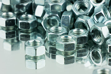 Stack of shiny nuts on a mirror background. Pile of fastener with a threaded hole that forms a connection with a screw, bolt or stud