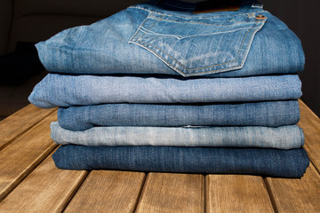 A stack of different pairs of blue jeans on a wooden table . Always in trend