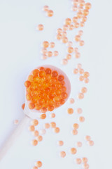 A wooden spoon with capsules similar to a red caviar on a white background, not isolated.