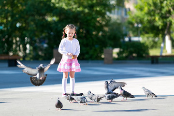 A little girl feeds pigeons. Beautiful girl gives bread to the birds on the city street.