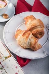 Close up shot of croissants on white plate next to cup of coffee with marshmallow and sweets .