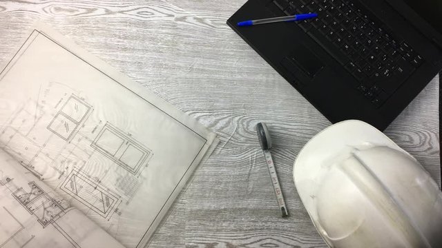 Escena de mesa de trabajo con planos, ordenados, casco de obra.