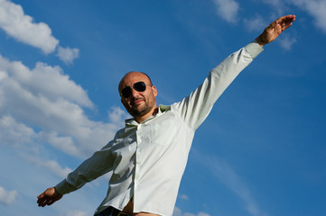 bearded businessman with sunglasses stretching his arms against the sky.
