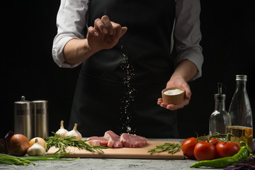 Pork steak and salt by the chef on the background. Horizontal photo. With vegetables, tomatoes, hot peppers, onions and chasnok. With black background