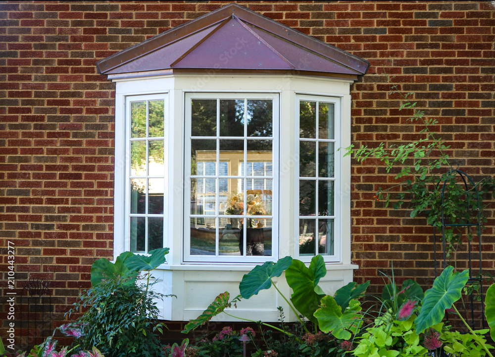 Wall mural bay window in a brick house with reflection of trees and view of windows and flowers inside and flow