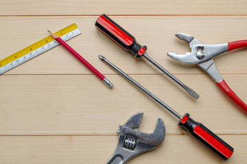 Top view and close up: Builder, repair and construction hand tool concept. There are red pliers, screwdrivers, wrenches pencil, ruler on wooden table background.