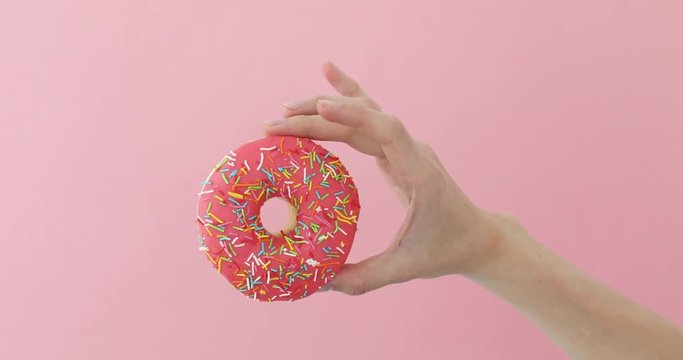 Womens hand holding pink donut on pink background