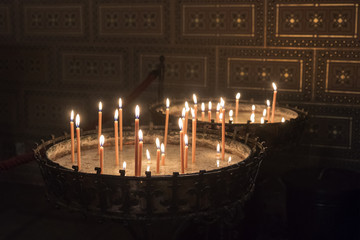 Candles lighted by prayers. Metal decorative circular containers with burning candles in the dark of Catholic Church. Prague, Czech Republic.
