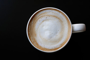 Top view of hot coffee latte cappuccino spiral foam in ceramic cup on dark background