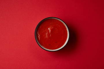 top view of tasty red tomato soup in plate on red table