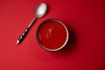 top view of tomato soup in plate and spoon on red surface