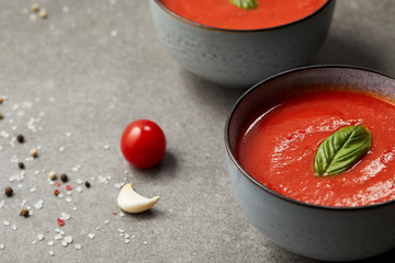 cooked tomato soup in plates and tomato with garlic on grey table