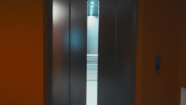 Young stylish Caucasian girl standing in elevator waving hand with closing doors. 4K UHD