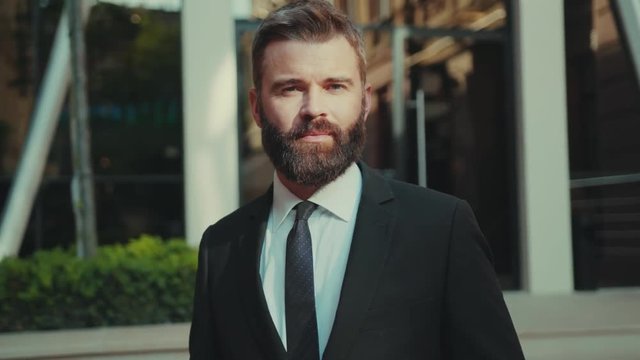 Portrait attractive businessman with beard standing look at camera smile outdoors sunset face technology successful boss company confident corporate happy marketing leadership young slow motion