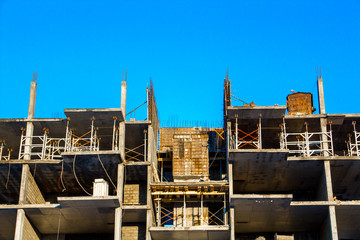 Fototapeta premium The frame of a highrise building under construction without walls against a blue clear sky. Abandoned building.