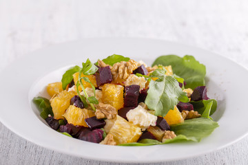 Healthy vegetarian salad with beetroot, green arugula, orange, feta cheese and walnuts on white plate
