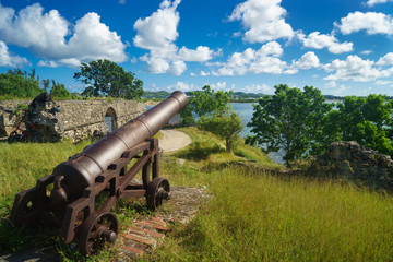 Old cannon in the fort is looking at sea with amazing clouds and island on background