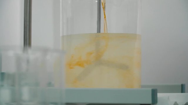 Chemist pouring orange liquid into a cup with mixing gel