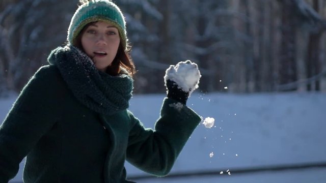 Slow-mo footage. Beautiful young girl throwing snowball at camera