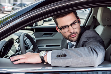 side view of pensive businessman in eyeglasses looking away while driving car
