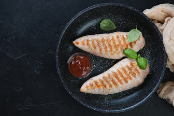Frying pan with barbecued turkey breast fillet, flatlay on a black stone background, horizontal shot with copyspace