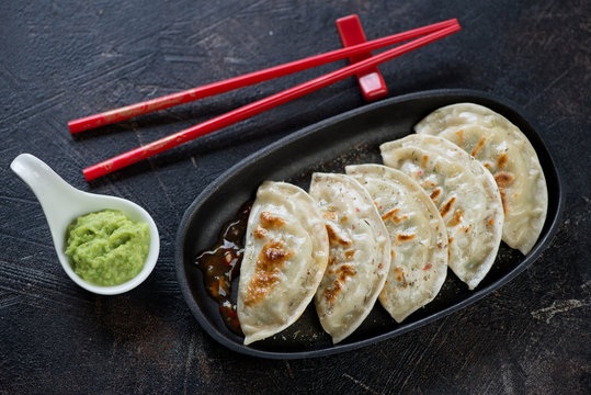 Cast-iron serving pan with potstickers or fried korean dumplings, high angle view on a dark brown stone surface
