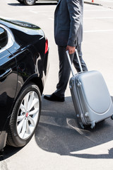  cropped image of businessman carrying wheeled bag near car at street