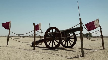 Cannon and flags of Qatar near Al Zubara Fort or Al Zubarah Fort - historic Qatari military fortress built in the time of Sheikh Abdullah bin Jassim Al Thani in 1938, Persian Gulf, Arabian Peninsula