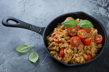 Cast-iron pan with couscous and cherry tomatoes over grey concrete background, studio shot