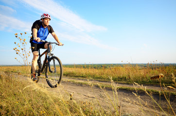 Fototapeta na wymiar Male cyclist with backpack driving by rural dirt road outdoors