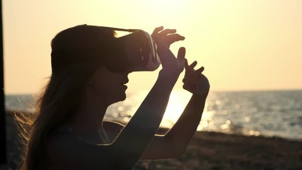 Young woman uses a virtual reality glasses on the beach. Sexy girl getting experience in using VR-headset at summer on sea background - Powered by Adobe