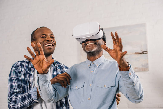 smiling young man looking at happy senior father using virtual reality headset