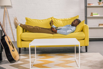senior african american man lying on sofa and using laptop