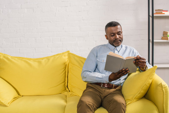 senior african american man sitting on sofa and reading book