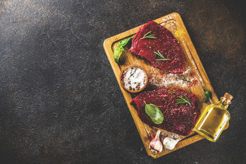 Raw beef meat with spices on cutting board, dark rusty background copy space