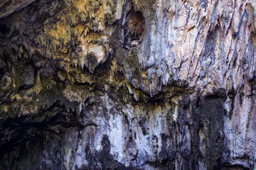 steep wall of the cave with stalactites and furrows, bright background of nature