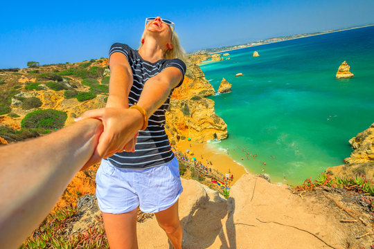 Follow me, woman holding hand at above promontory of Praia Do Camilo in Algarve, Portugal, Europe. Woman freedom at Camilo Beach. Concept of summer holidays and tourist traveler, holding man by hand.