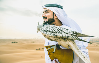 Fototapeta premium Arabski mężczyzna w tradycyjnych emirackich strojach spacerujący po pustyni ze swoim sokołem