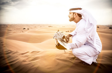 Obraz premium Arabski mężczyzna w tradycyjnych emirackich strojach spacerujący po pustyni ze swoim sokołem